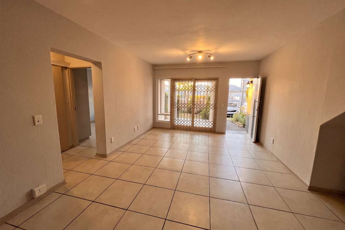 An empty, open-plan living area featuring neutral tiled flooring, recessed lighting, and a sliding security gate leading to the exterior.