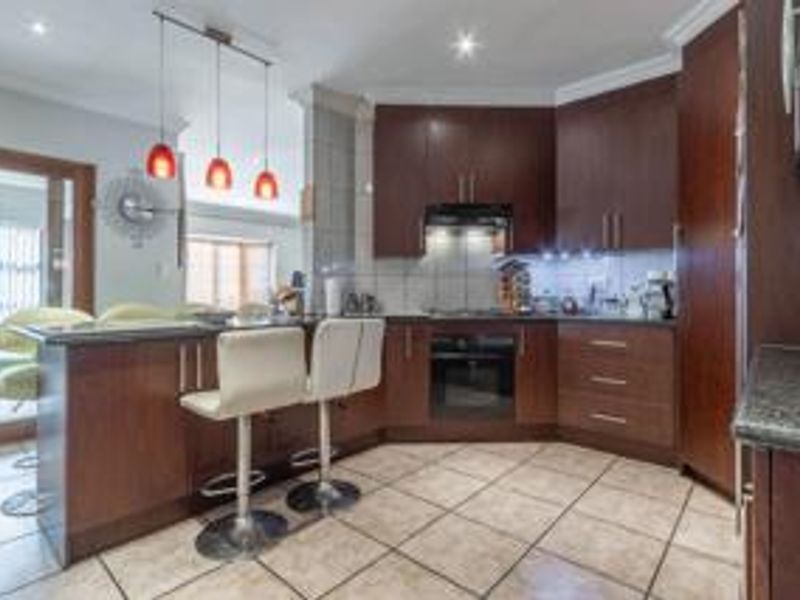 Modern kitchen featuring dark wood cabinetry, granite countertops, built-in appliances, and a breakfast bar, seamlessly connected to the adjacent living area.