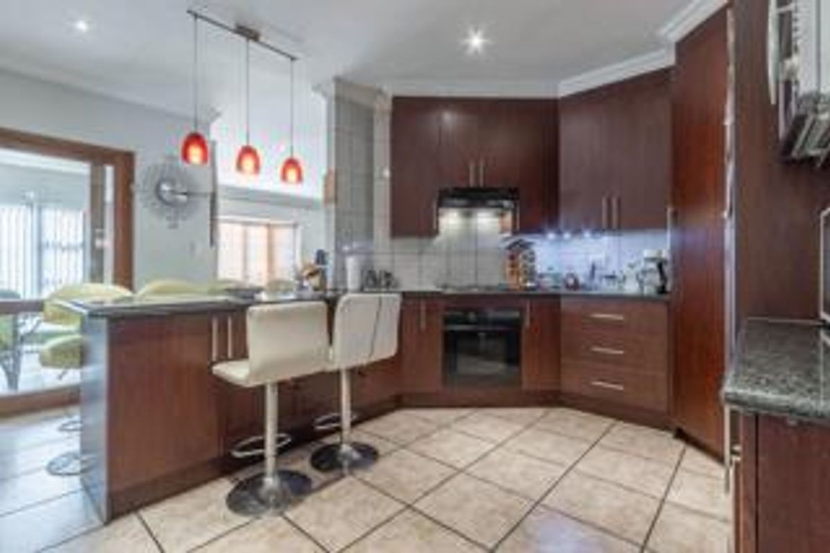 Modern kitchen featuring dark wood cabinetry, granite countertops, built-in appliances, and a breakfast bar, seamlessly connected to the adjacent living area.