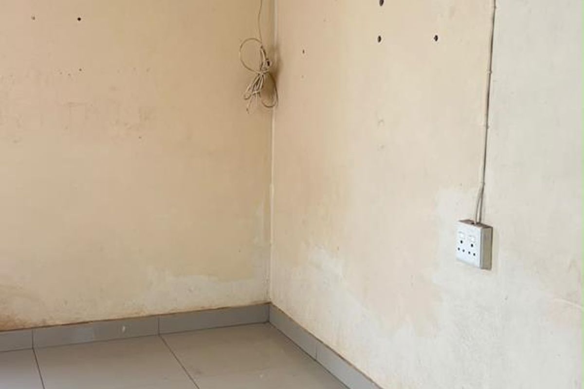 An empty living area featuring tiled flooring, decorative ceiling tiles, and wall surfaces requiring cosmetic attention and repair.