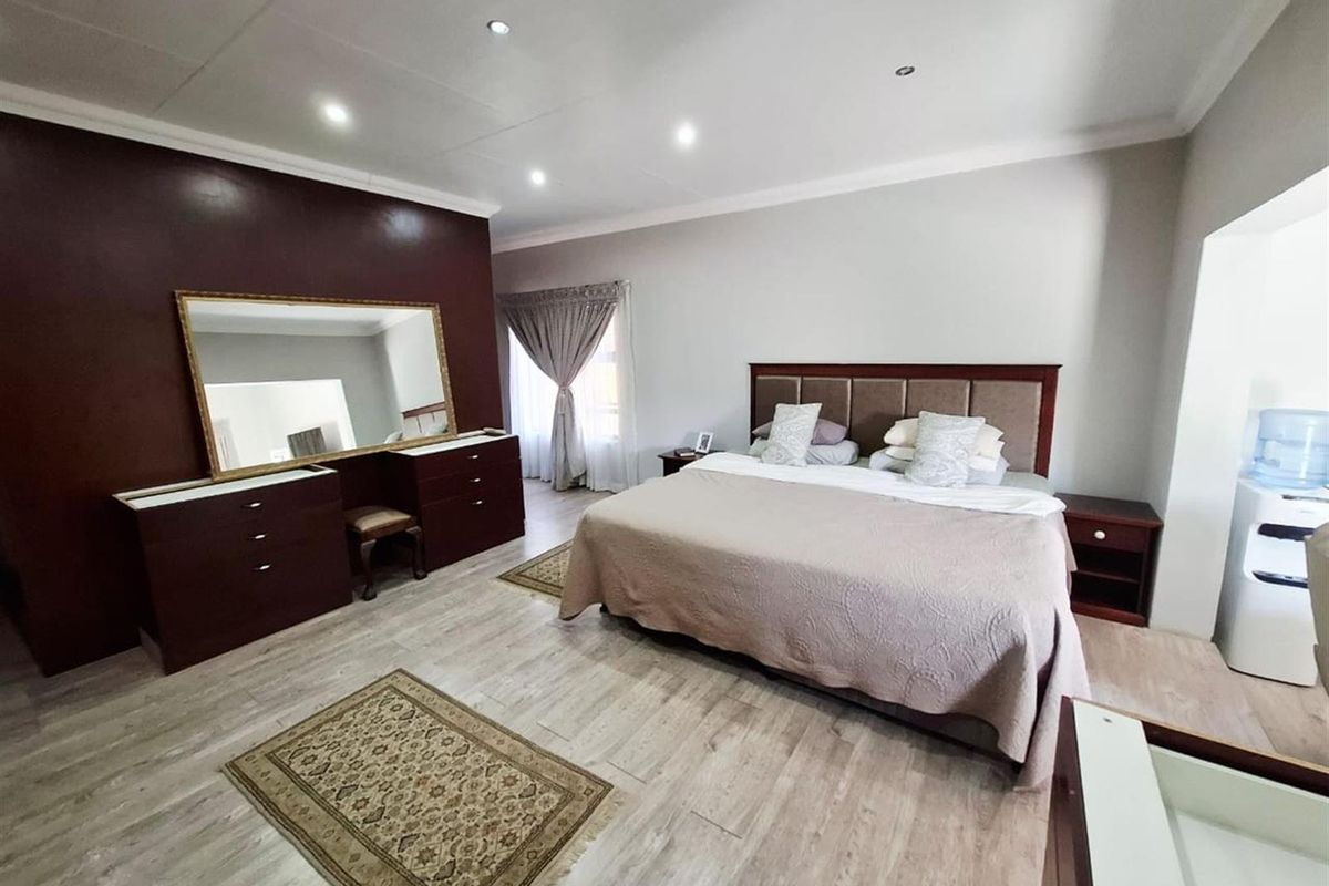 Spacious bedroom featuring laminate flooring, recessed downlighting, and a neutral color palette with a dark accent wall.