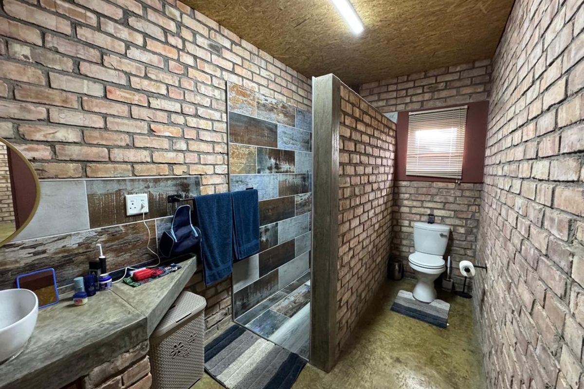 A rustic-style bathroom featuring exposed brick walls, a concrete vanity, a walk-in shower with decorative tiling, and a separate toilet area.
