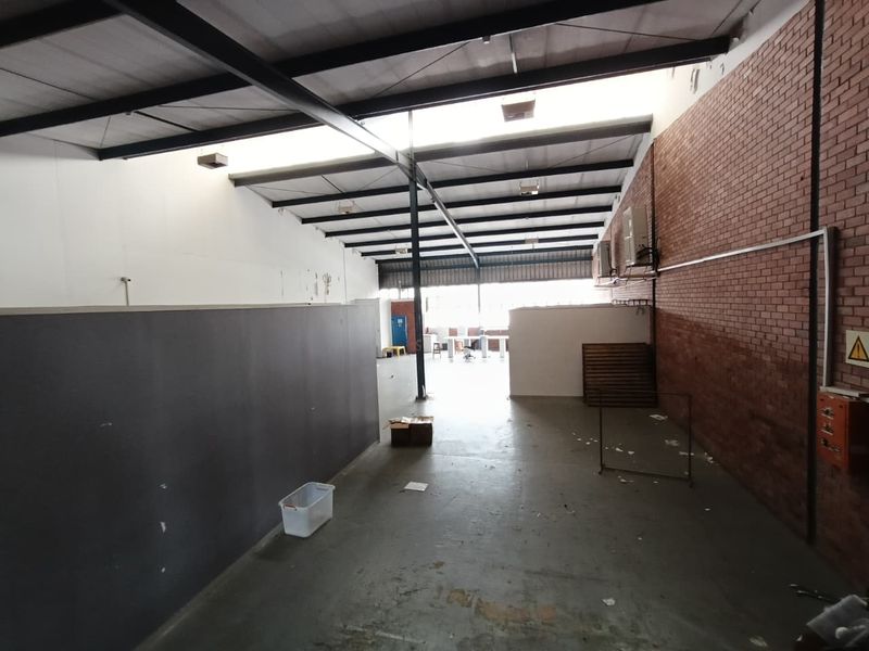 Spacious industrial utility area featuring exposed steel roof trusses, brick wall detailing, concrete flooring, and wall-mounted air conditioning units.