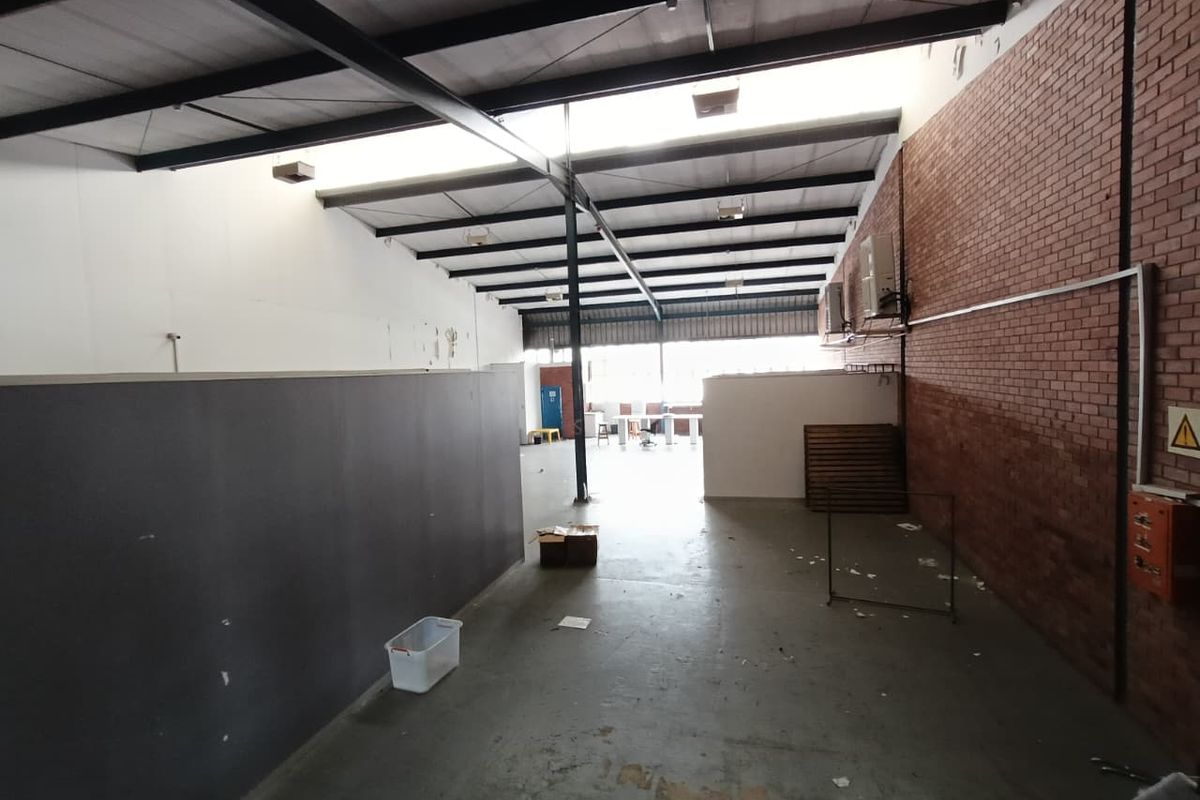 Spacious industrial utility area featuring exposed steel roof trusses, brick wall detailing, concrete flooring, and wall-mounted air conditioning units.