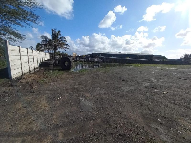 An expansive industrial yard area featuring a precast concrete boundary wall and metal fencing, with visible ground surface and drainage considerations.