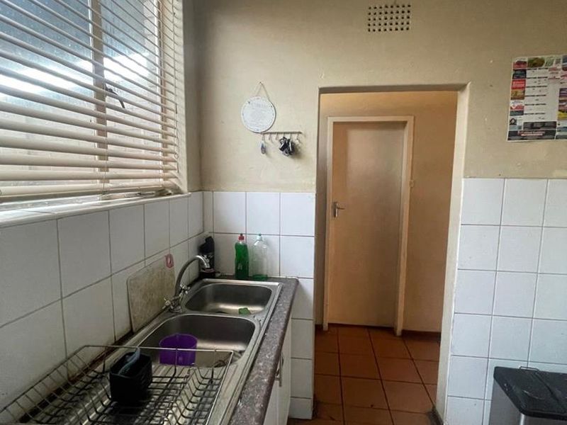 A functional scullery area featuring a double basin stainless steel sink, tiled splashbacks, and ceramic floor tiles, offering practical utility space.