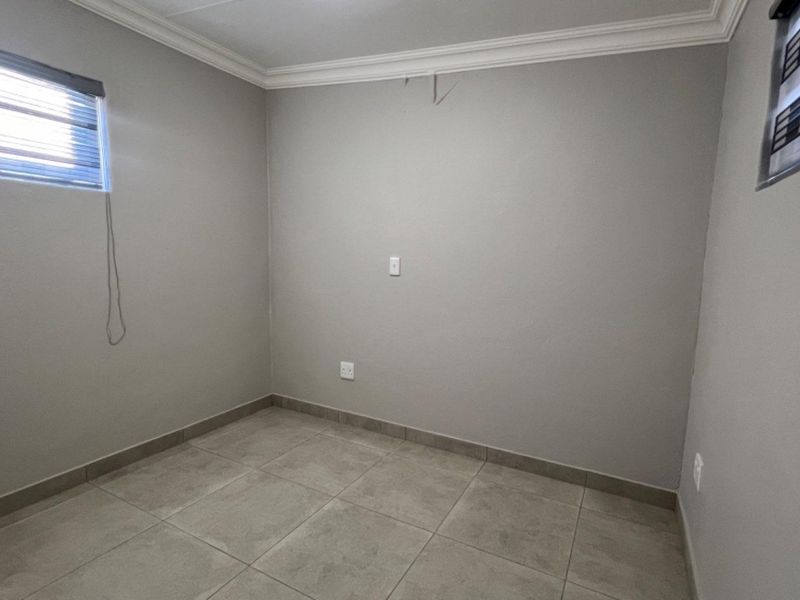 An empty bedroom featuring neutral grey walls, tiled flooring, and fitted blinds, ready for personalization.