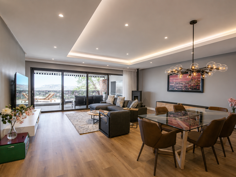 Spacious open-plan living and dining area featuring modern recessed lighting, wood-look flooring, and large sliding glass doors leading to a scenic balcony.