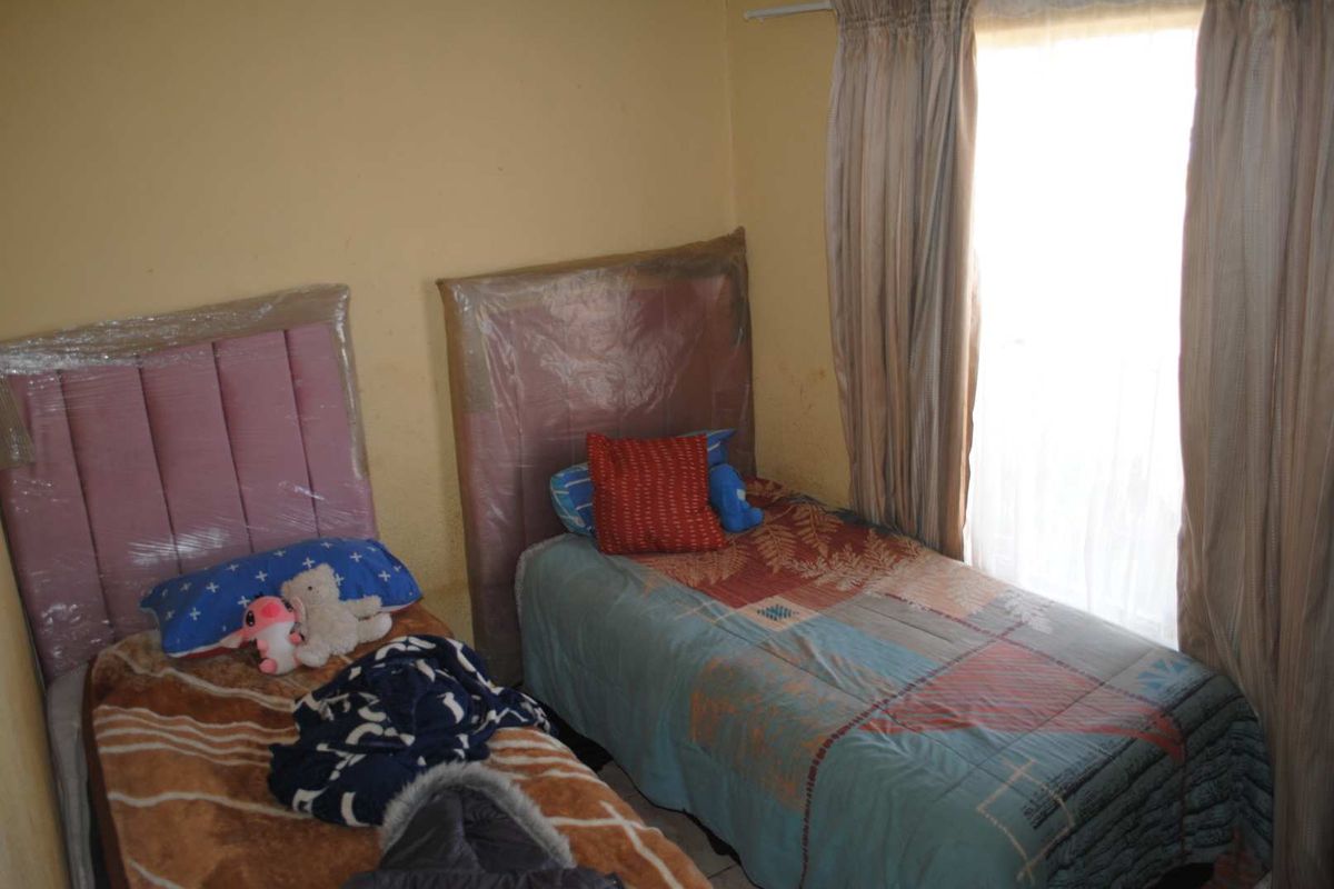 A bedroom featuring two single beds, neutral wall paint, and window curtains.