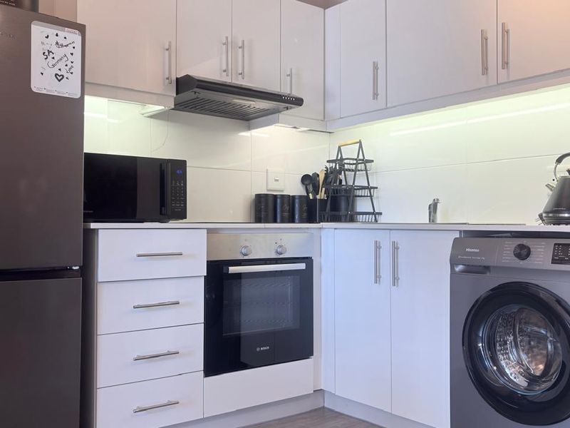 Modern kitchen featuring white cabinetry, tiled backsplash, built-in oven, extractor fan, and integrated space for a washing machine.