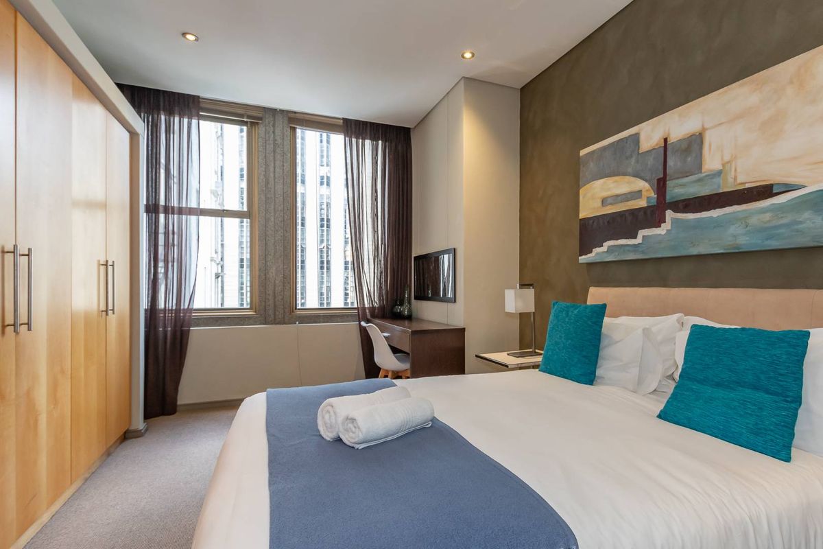 A well-maintained bedroom featuring built-in wooden wardrobes, recessed lighting, and large windows providing natural light and urban views.