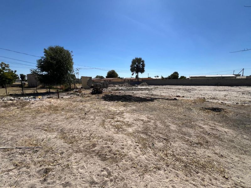 A large, undeveloped plot of land featuring sandy terrain, perimeter walling, and sparse vegetation, offering a blank canvas for future development.