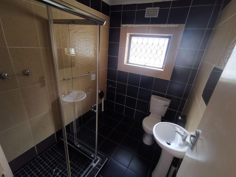 A functional bathroom featuring a shower enclosure, pedestal basin, and toilet, finished with contrasting black and beige wall and floor tiles.