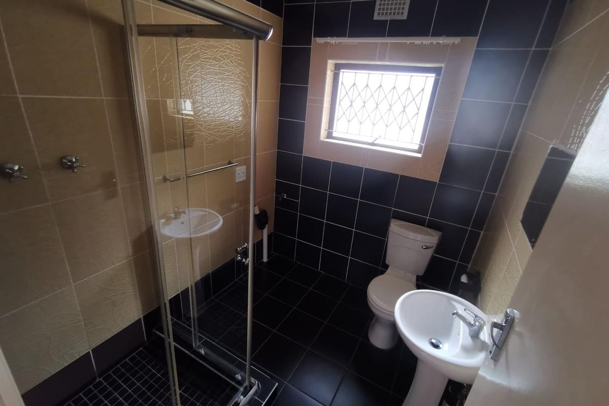 A functional bathroom featuring a shower enclosure, pedestal basin, and toilet, finished with contrasting black and beige wall and floor tiles.