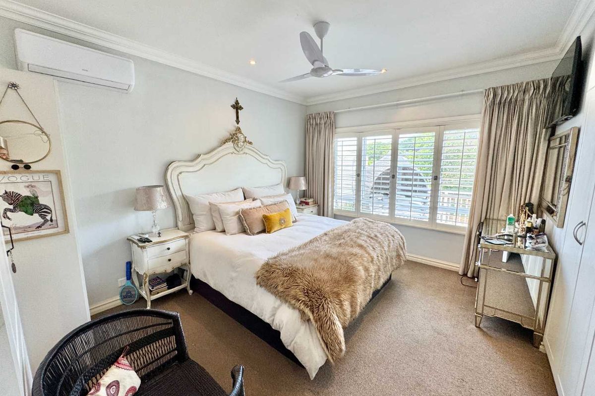 A well-maintained bedroom featuring a ceiling fan, wall-mounted air conditioning unit, and plantation shutters on the windows.