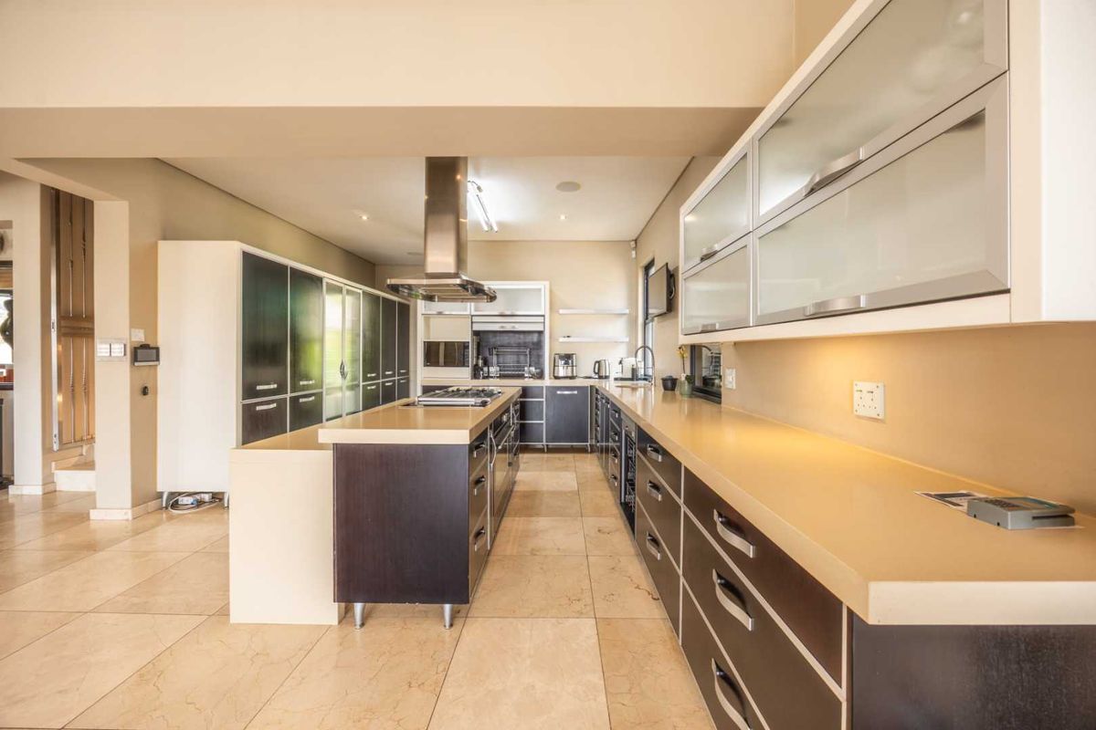 Modern kitchen featuring a central island, stone countertops, built-in cabinetry, stainless steel extractor fan, and tiled flooring.