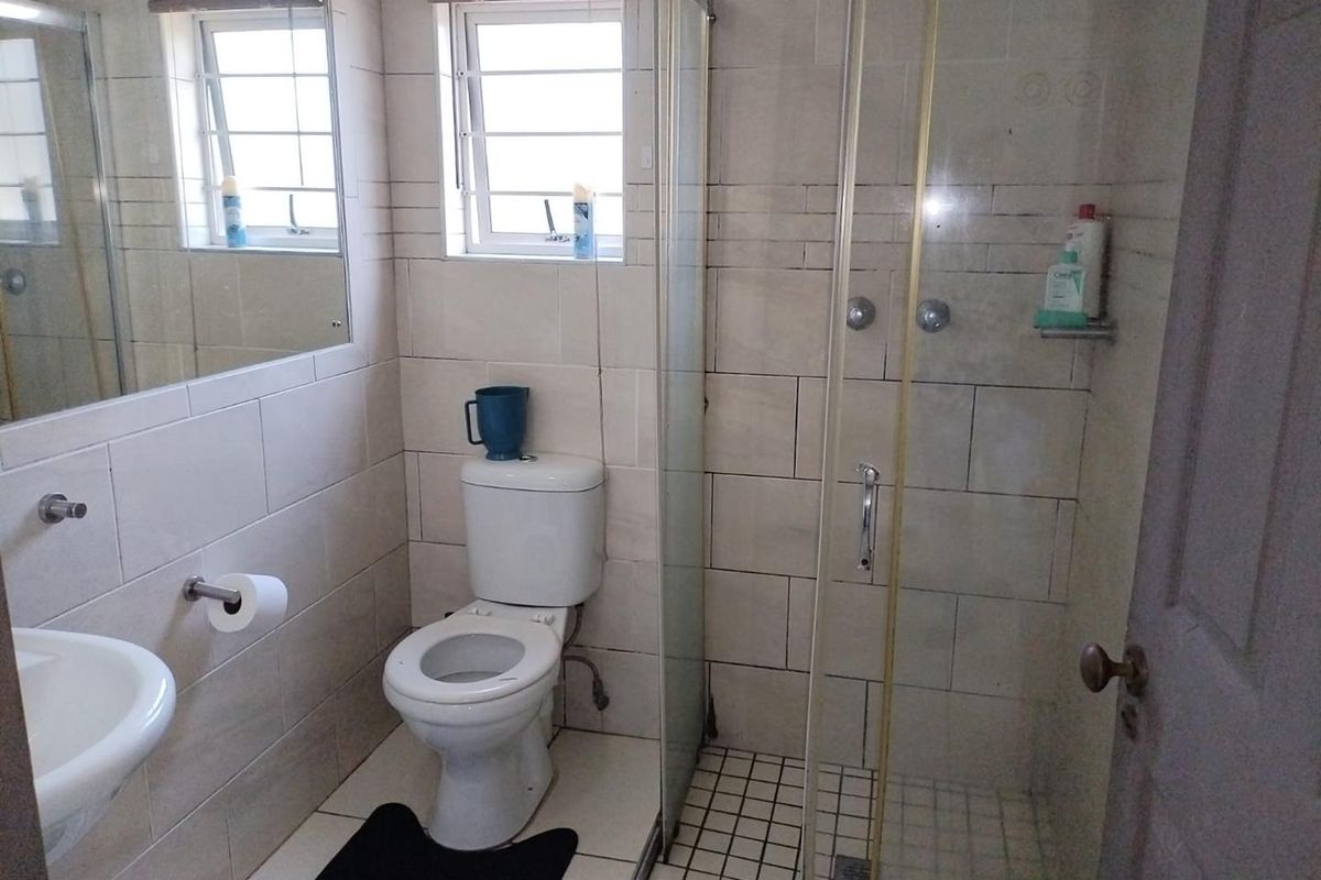A functional bathroom featuring a glass shower enclosure, wall-mounted basin, toilet, and neutral wall tiling with natural light from a window.