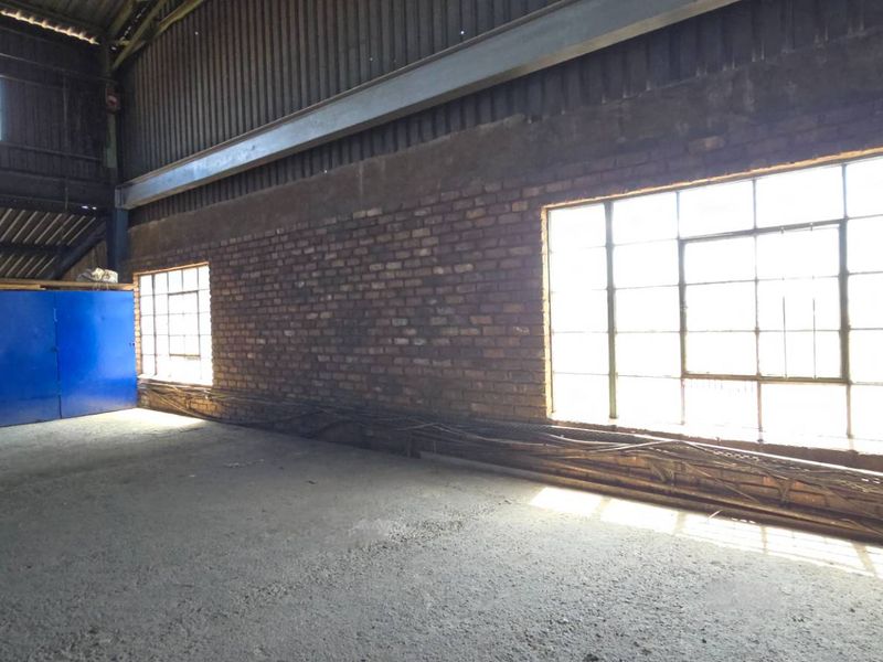 Spacious industrial utility area featuring exposed brick walls, large steel-framed windows, concrete flooring, and high-volume exposed steel roof structure.