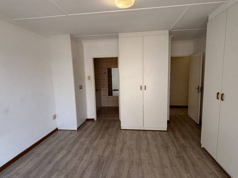 A vacant bedroom featuring laminate flooring and extensive built-in cupboard storage, offering a neutral canvas for personalization.