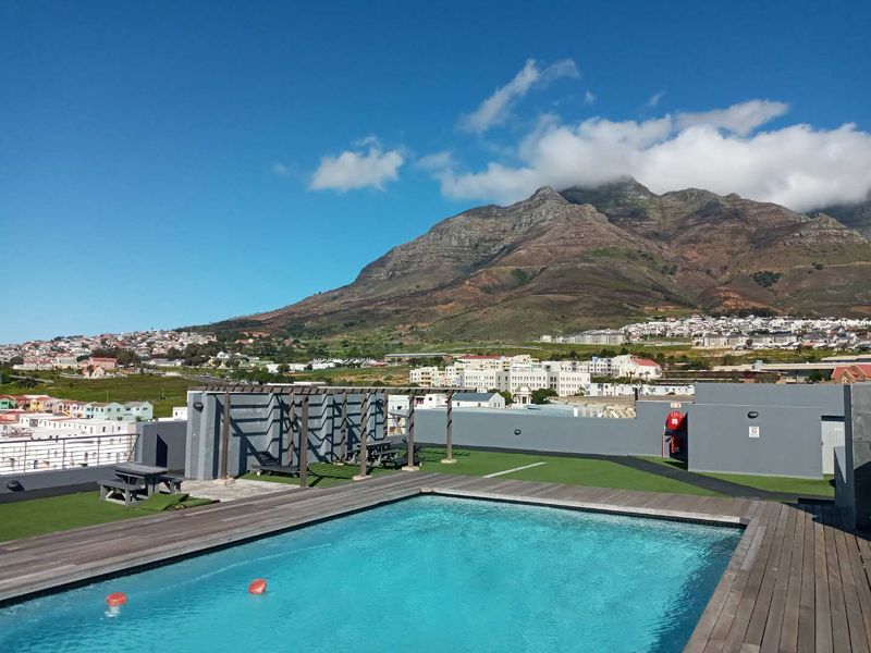 Rooftop swimming pool area featuring timber decking, artificial grass, and a pergola, offering expansive mountain and urban views.