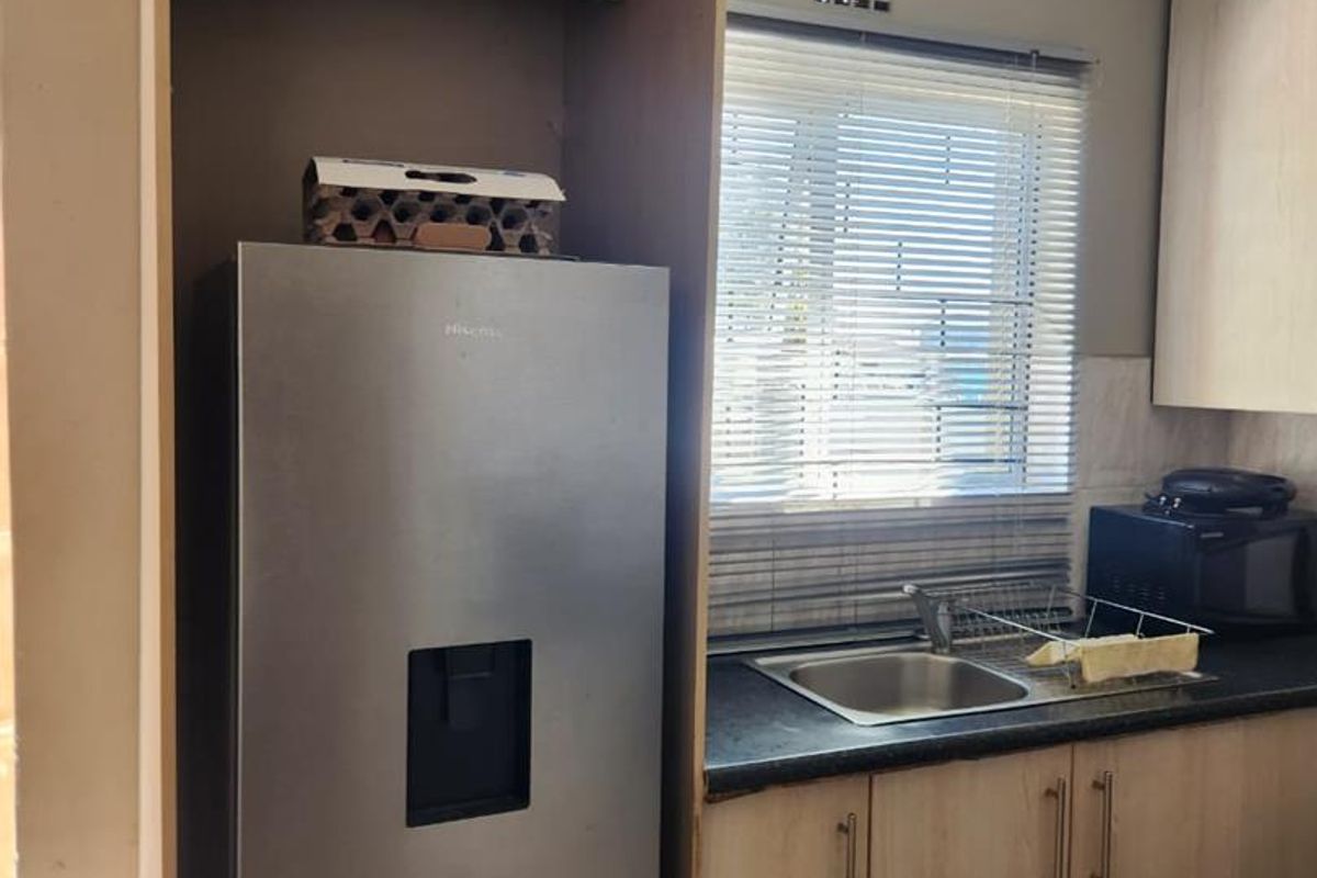 A functional kitchen area featuring light wood-finish cabinetry, dark laminate countertops, a stainless steel sink, and tiled flooring.