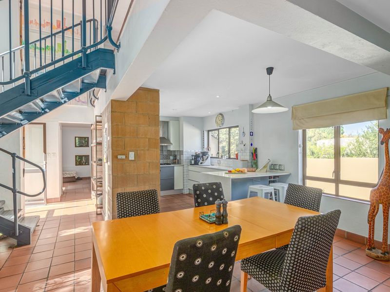 Open-plan living and dining area featuring a prominent staircase, exposed brick pillar, and a functional kitchen with island and tiled flooring.