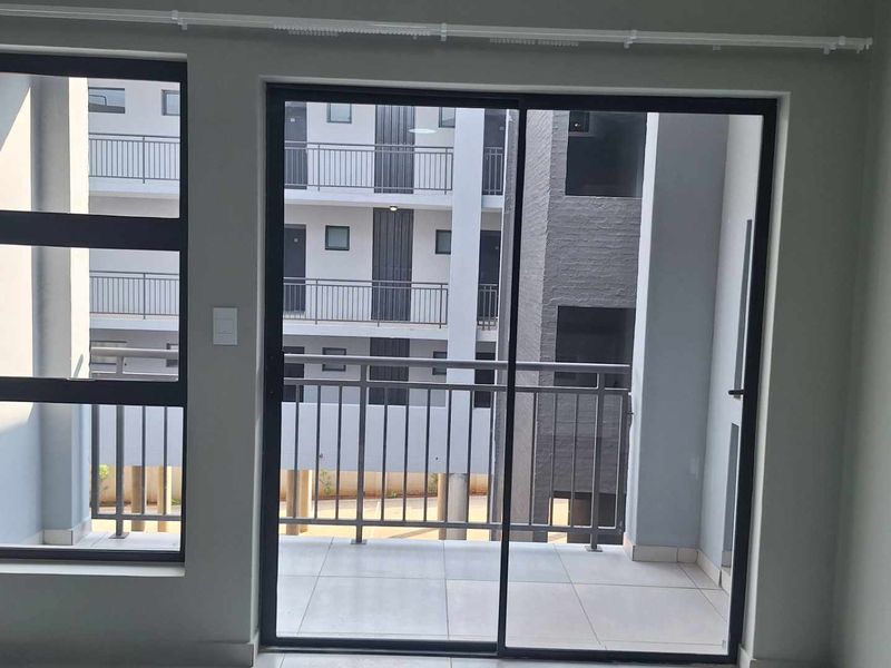 A view from an interior room looking out onto a tiled balcony with a metal balustrade, overlooking a modern apartment complex courtyard.
