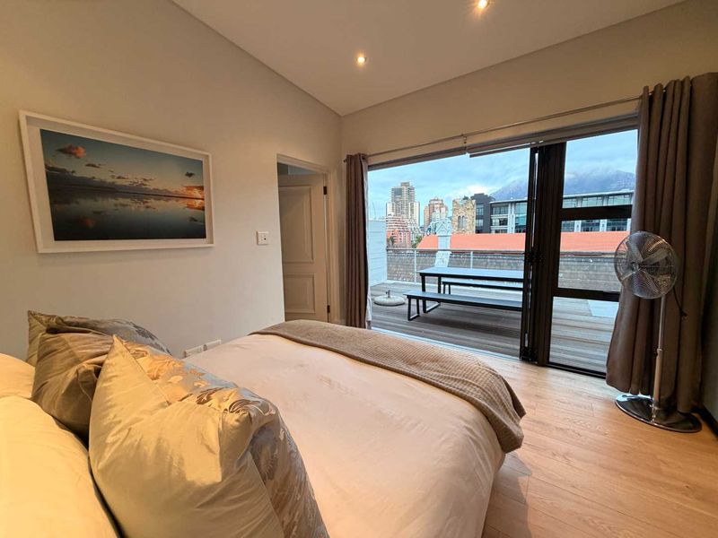 A well-maintained bedroom featuring laminate flooring, recessed lighting, and large stacking glass doors that open onto a private timber deck with city views.