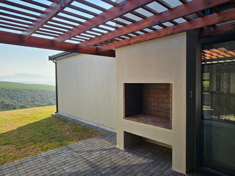 Covered patio area featuring a wooden pergola, built-in brick fireplace, and paved flooring, offering scenic landscape views.