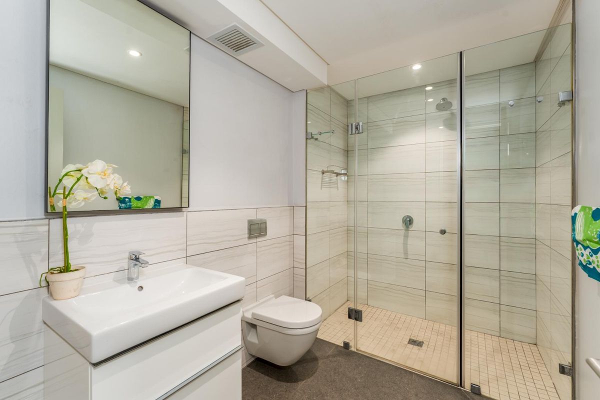 Modern bathroom featuring a wall-mounted toilet, vanity with basin, large mirror, and a spacious walk-in glass shower enclosure with tiled finishes.