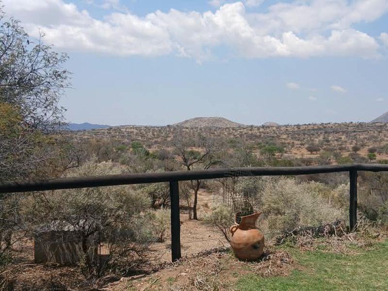 A scenic elevated view overlooking a vast arid landscape with distant hills, framed by a rustic timber post and rail fence.
