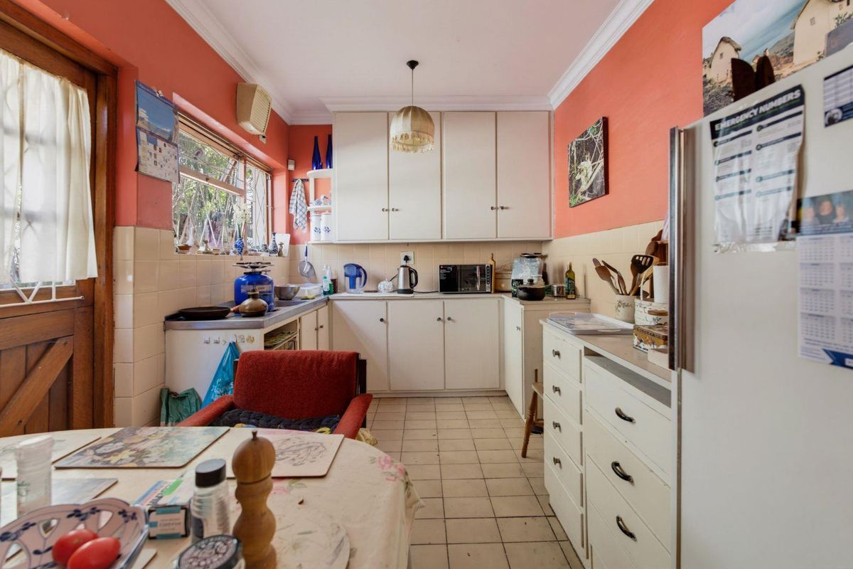 A dated kitchen featuring white cabinetry, tiled splashbacks, and tiled flooring, offering a functional layout with direct access to the exterior.