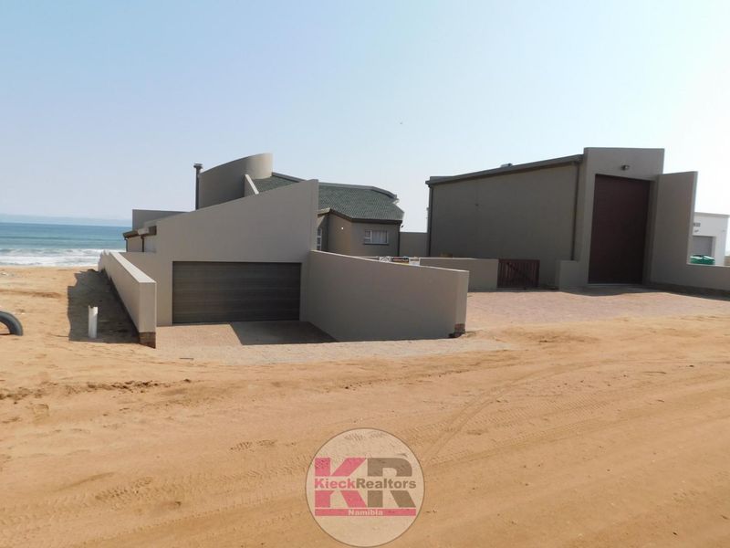 A modern coastal property featuring a garage, paved driveway, and boundary walls, situated directly along the beachfront.