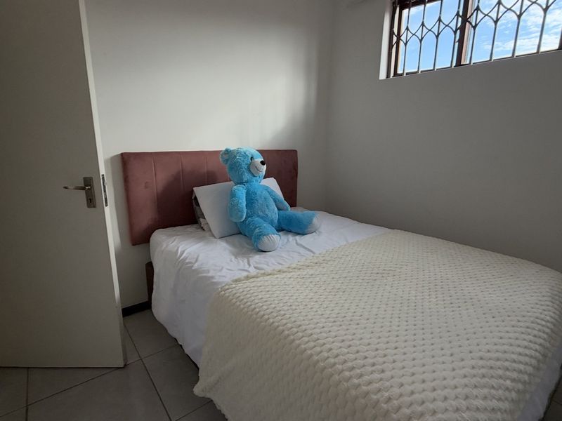 A compact bedroom featuring tiled flooring and a window fitted with security bars, providing a functional and secure living space.