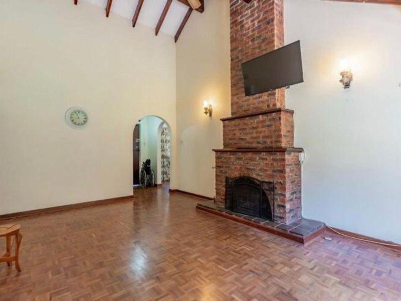 Spacious living room featuring high vaulted ceilings with exposed timber beams, a prominent brick fireplace, and classic parquet flooring.