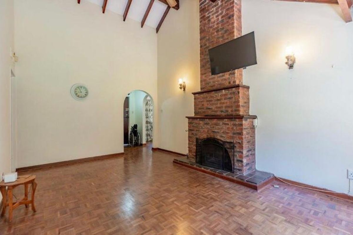Spacious living room featuring high vaulted ceilings with exposed timber beams, a prominent brick fireplace, and classic parquet flooring.