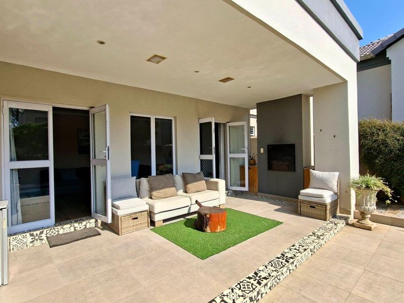 A covered patio area featuring tiled flooring, a built-in fireplace, and direct access to the interior through double glass doors.
