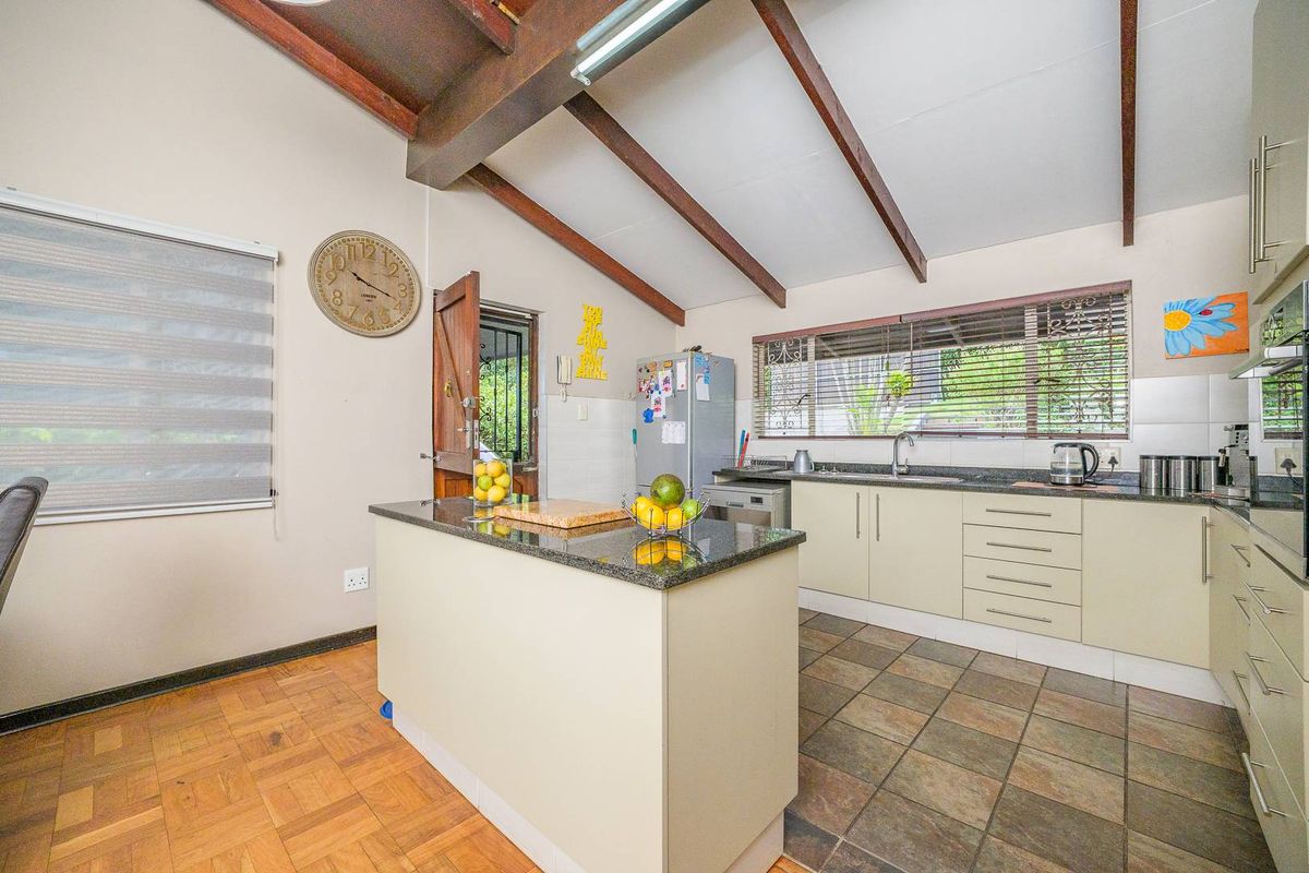 A functional kitchen featuring granite countertops, a central island, exposed timber ceiling beams, and a mix of tiled and parquet flooring.