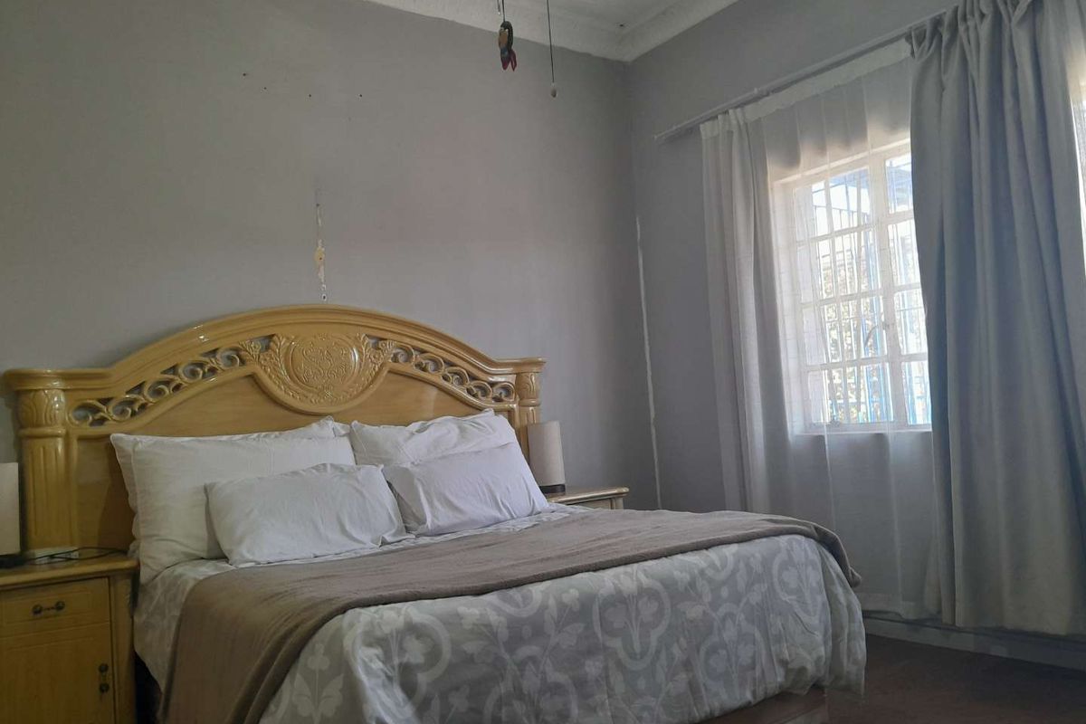 A bedroom featuring an ornate ceiling cornice and a window fitted with security bars, showing signs of wear on the wall surfaces.