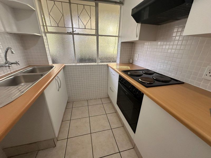 A compact, functional kitchen featuring white cabinetry, laminate countertops, a double sink, and built-in cooking appliances with tiled splashbacks.
