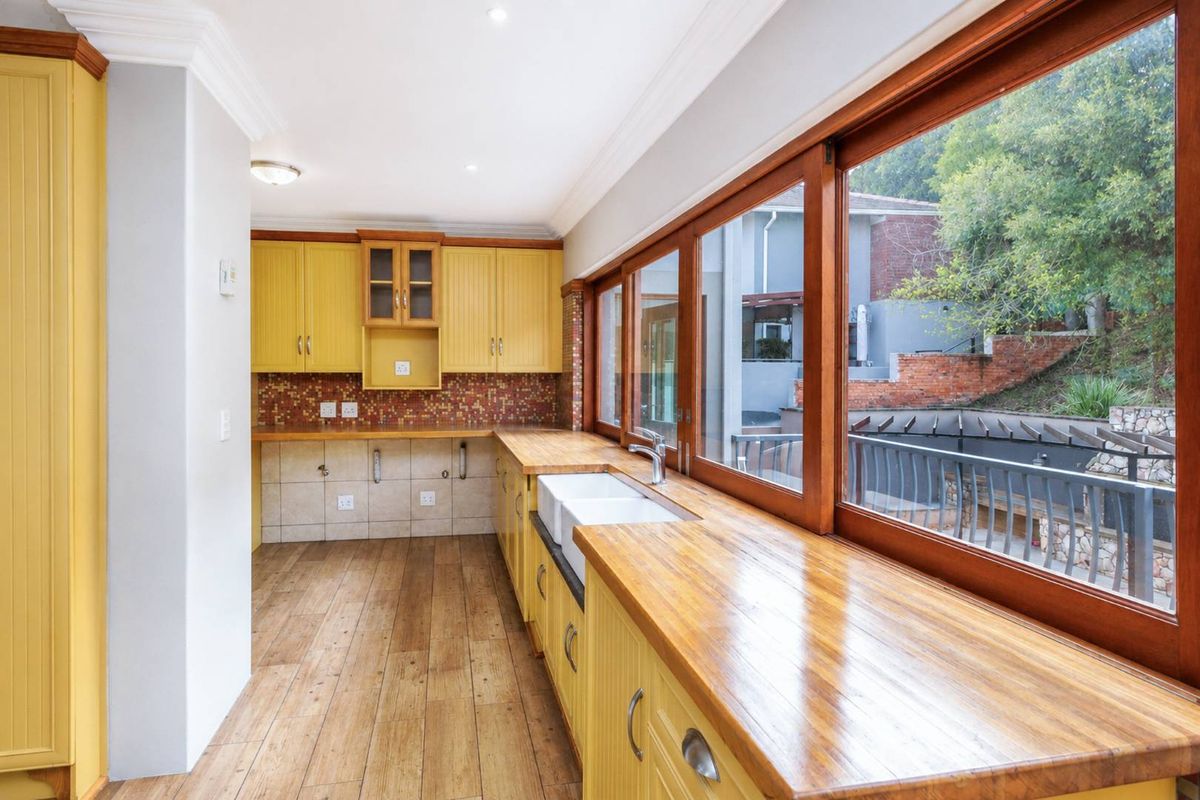 A bright kitchen featuring yellow cabinetry, wooden countertops, a double farmhouse sink, and large timber-framed windows overlooking the rear garden area.