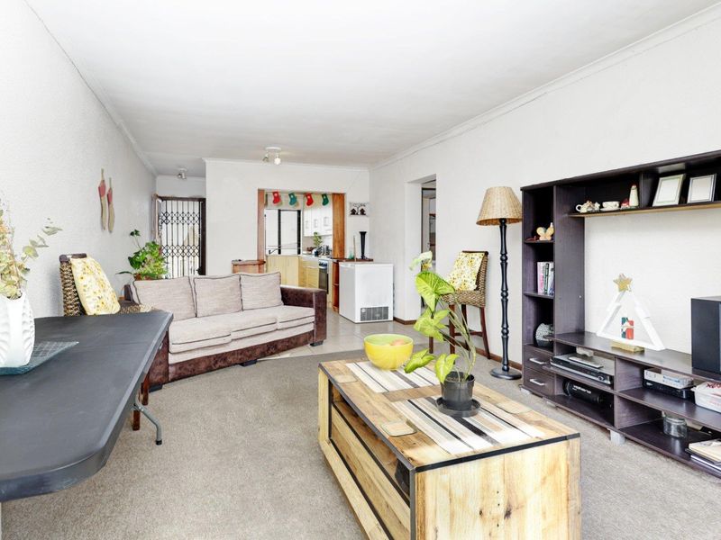 Open plan living area featuring carpeted flooring and coved ceilings, with a view through to the kitchen area.