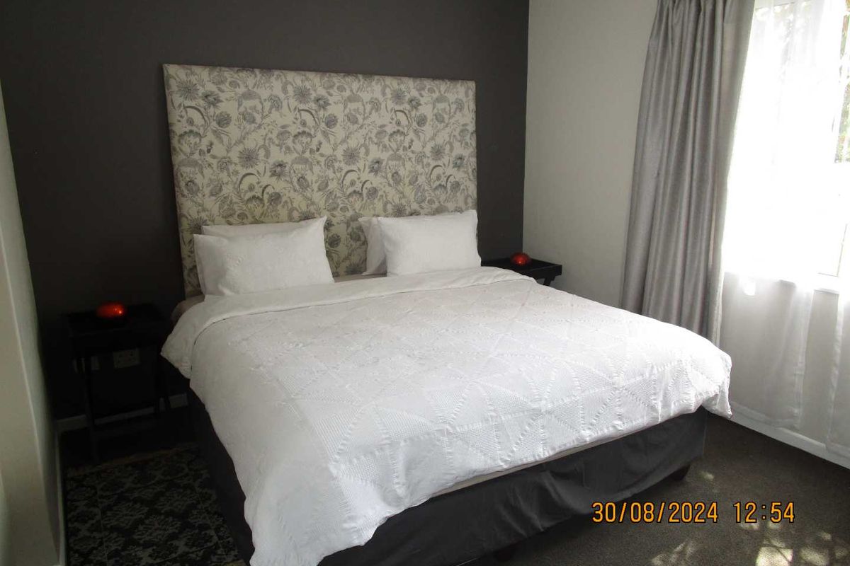 A well-lit bedroom featuring a neutral color palette, carpeted flooring, and a large window with curtains.