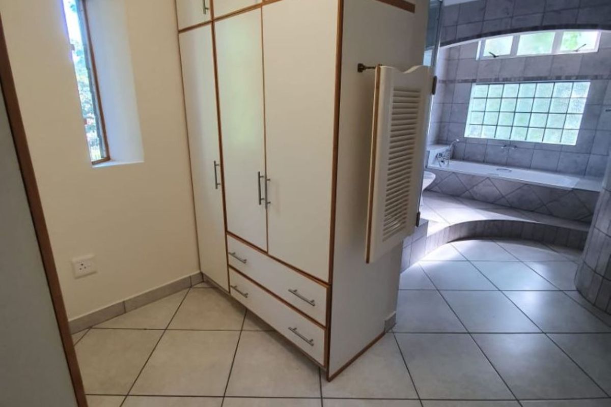 A bathroom area featuring built-in cabinetry, tiled flooring, and a sunken bathtub with a glass block window feature.