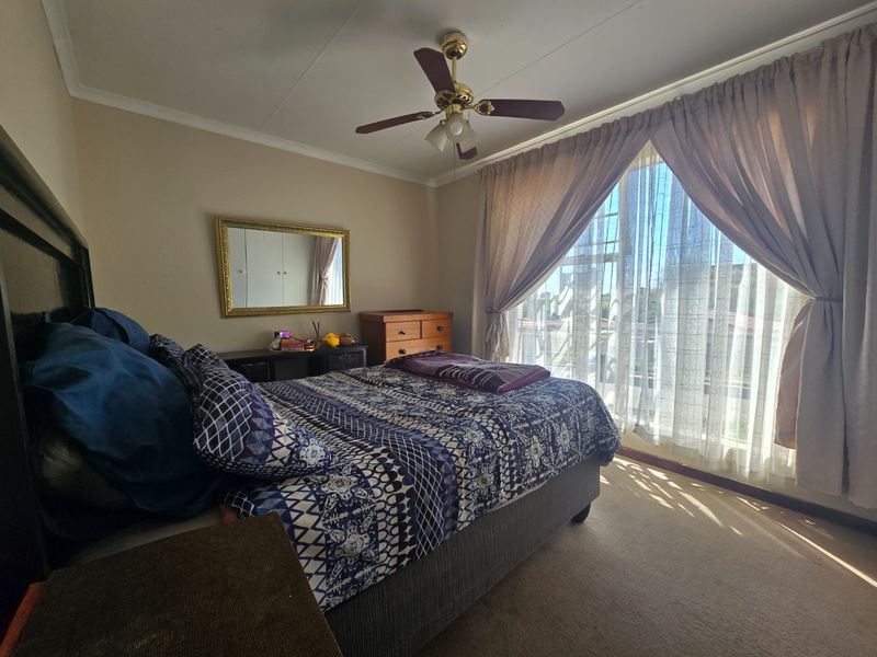 A standard bedroom featuring carpeted flooring, a ceiling fan, and large windows with curtain treatments, offering a functional and lived-in space.