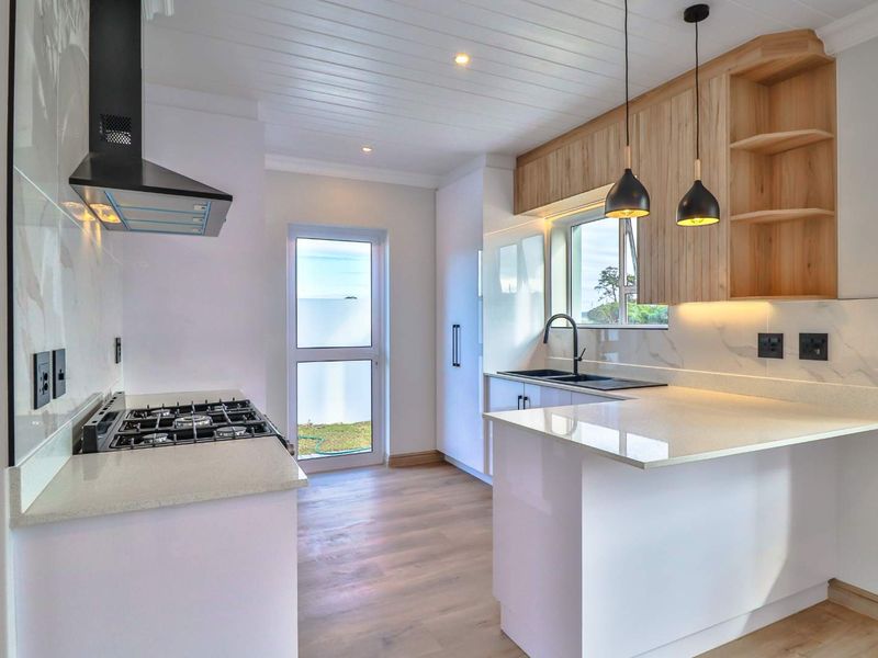 Modern kitchen featuring stone countertops, gas hob, extractor fan, and sleek cabinetry with integrated lighting and wood-look laminate flooring.