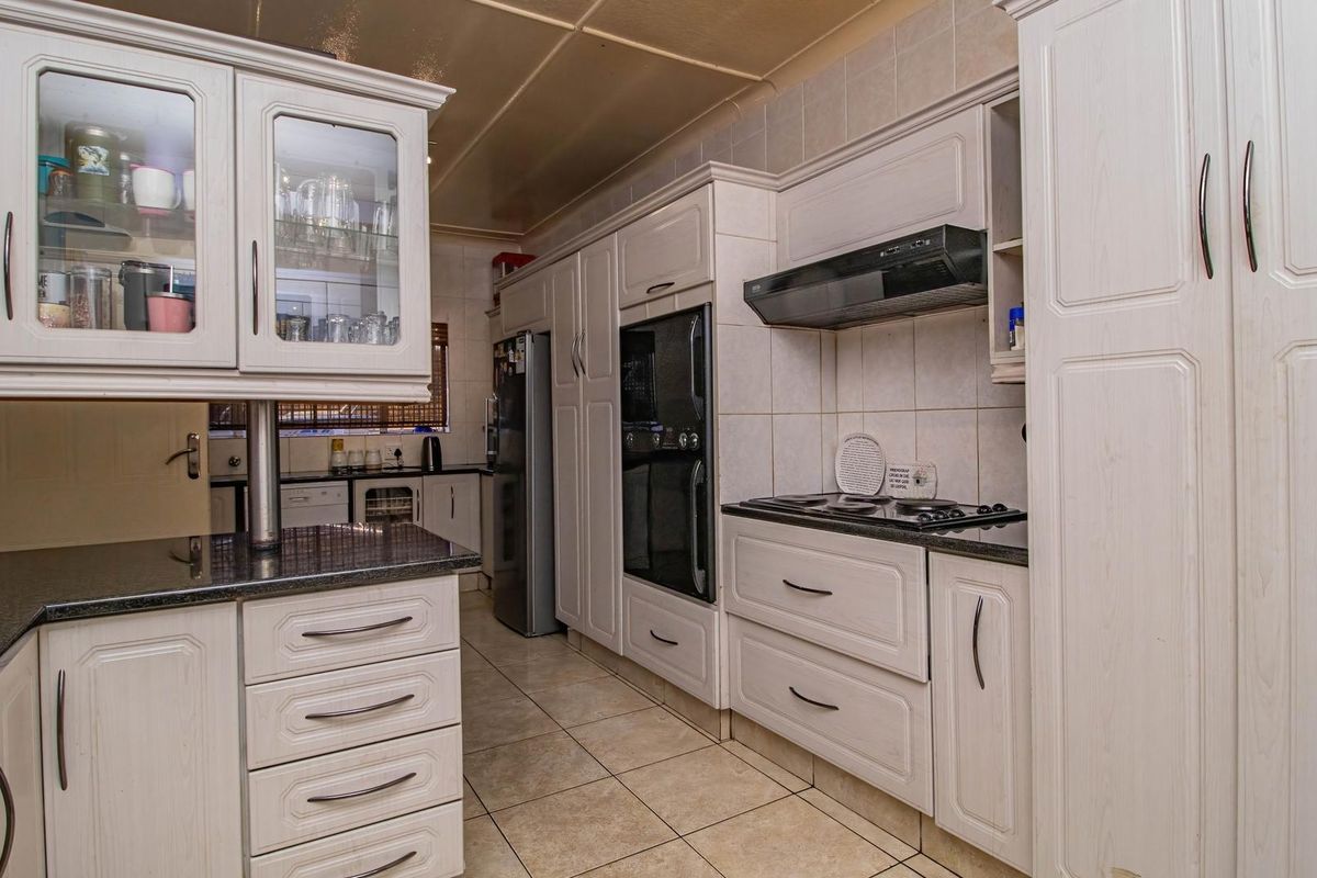 A functional kitchen featuring light-toned cabinetry, granite countertops, built-in oven, and a fitted extractor fan with tiled flooring.