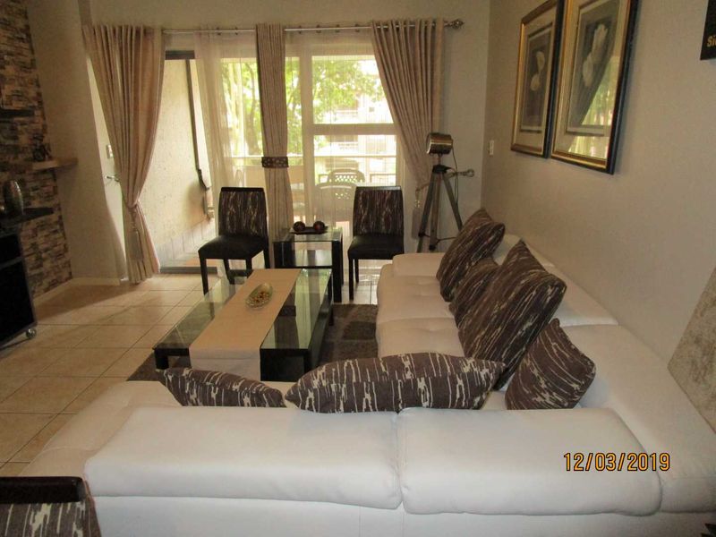 A comfortable living room featuring tiled flooring, a stone accent wall, and a sliding glass door providing access to the balcony.