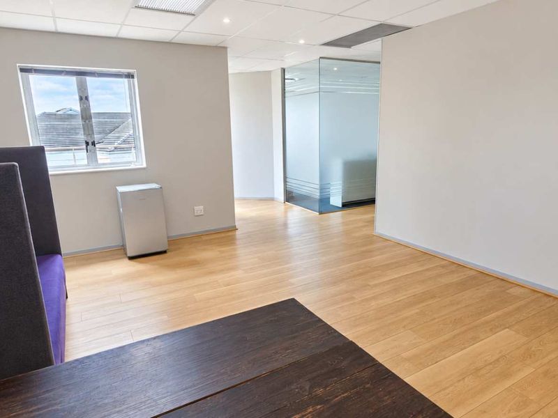 A bright, modern office space featuring laminate flooring, a suspended ceiling, and a contemporary glass partition wall, offering a clean and professional work environment.