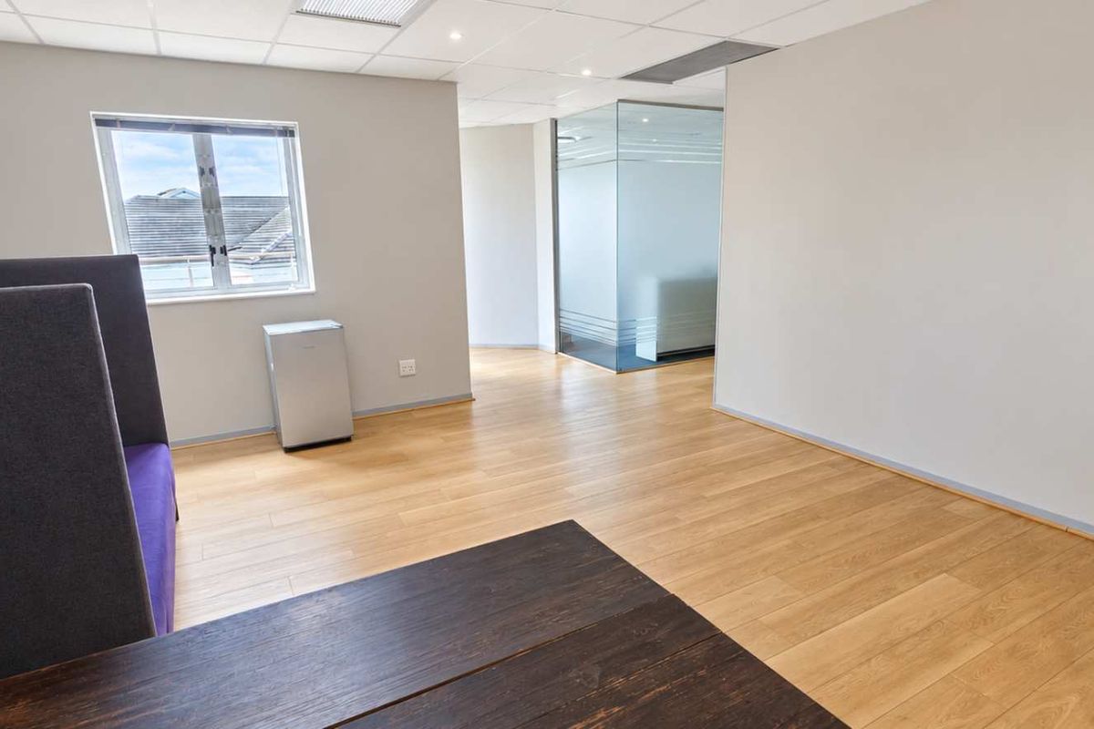 A bright, modern office space featuring laminate flooring, a suspended ceiling, and a contemporary glass partition wall, offering a clean and professional work environment.